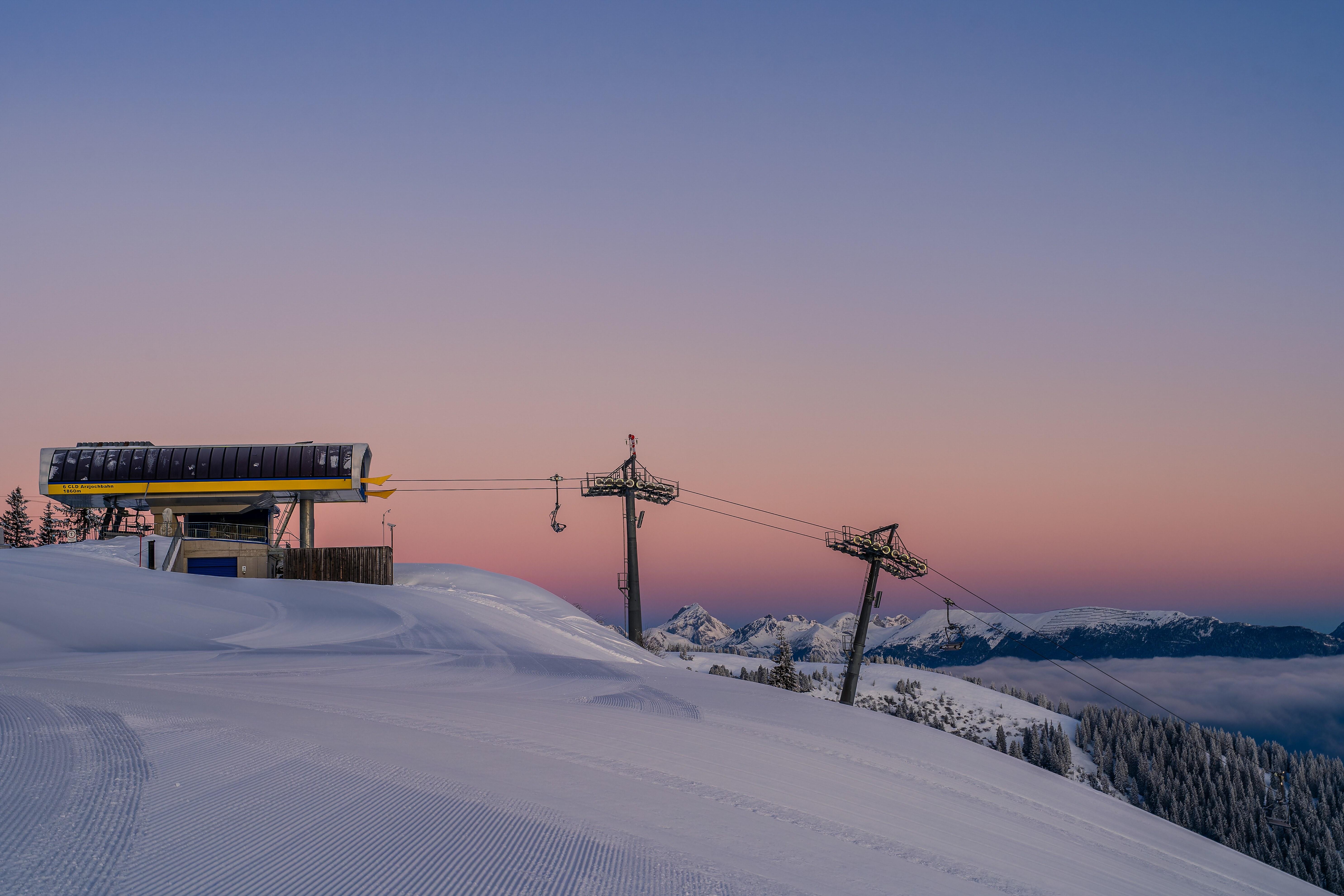Präparierte Skipiste am Onkeljoch mit Liftanlage und verschneiten Bergen im Morgenlicht